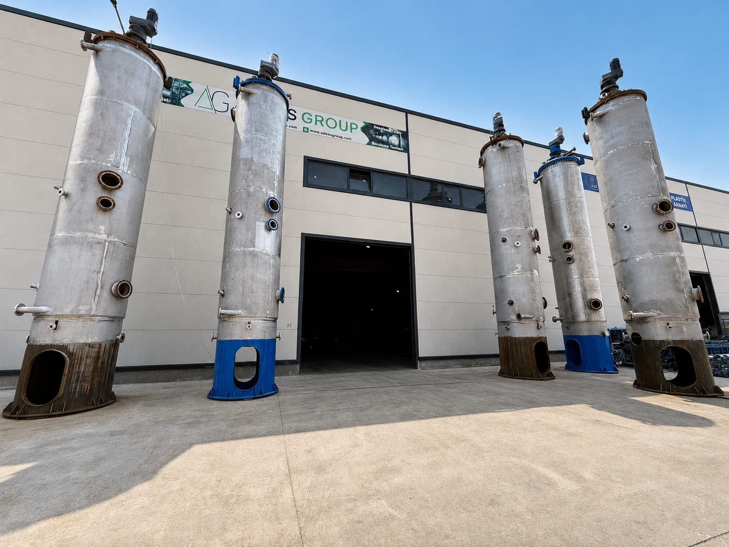 Row of stainless steel absorber columns standing outside the ADESS fabrication hall